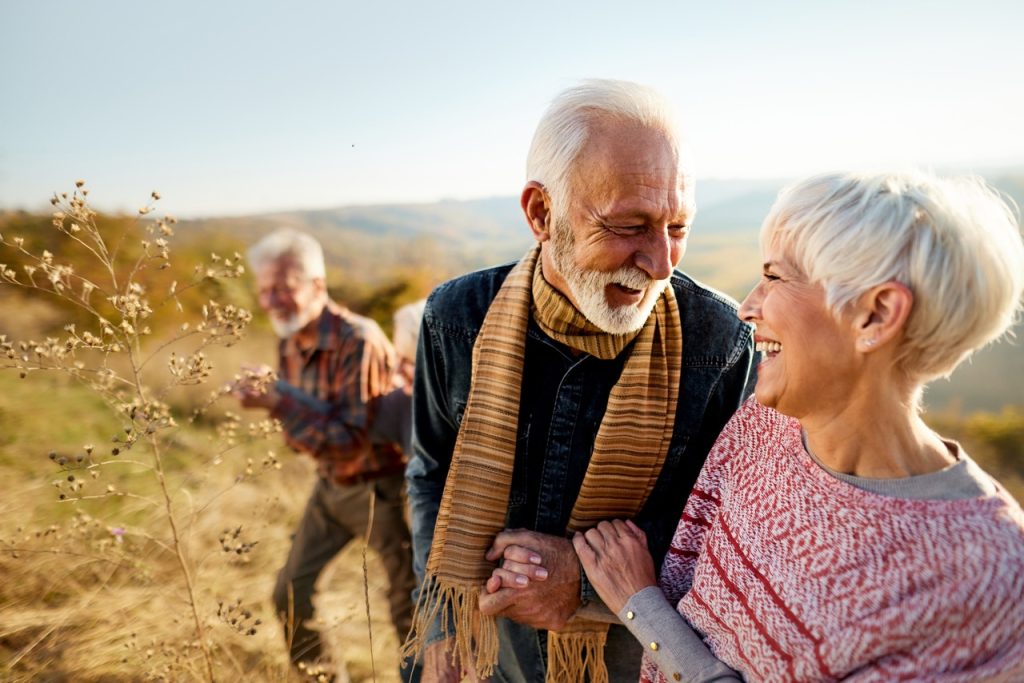 Happy mature couple communicating while walking with their friends in autumn day. Copy space.