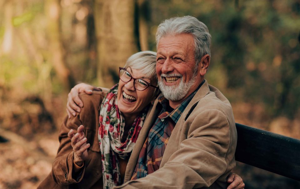Old couple people holding each other on a bench in an autumnal forrest.
