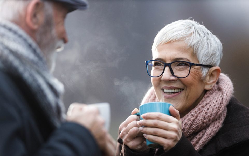 Elderly couple outside in the cold enjoying a hot drink.