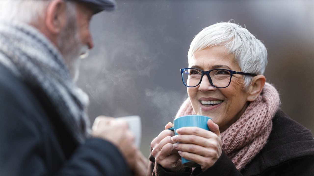 Elderly couple outside in the cold enjoying a hot drink.