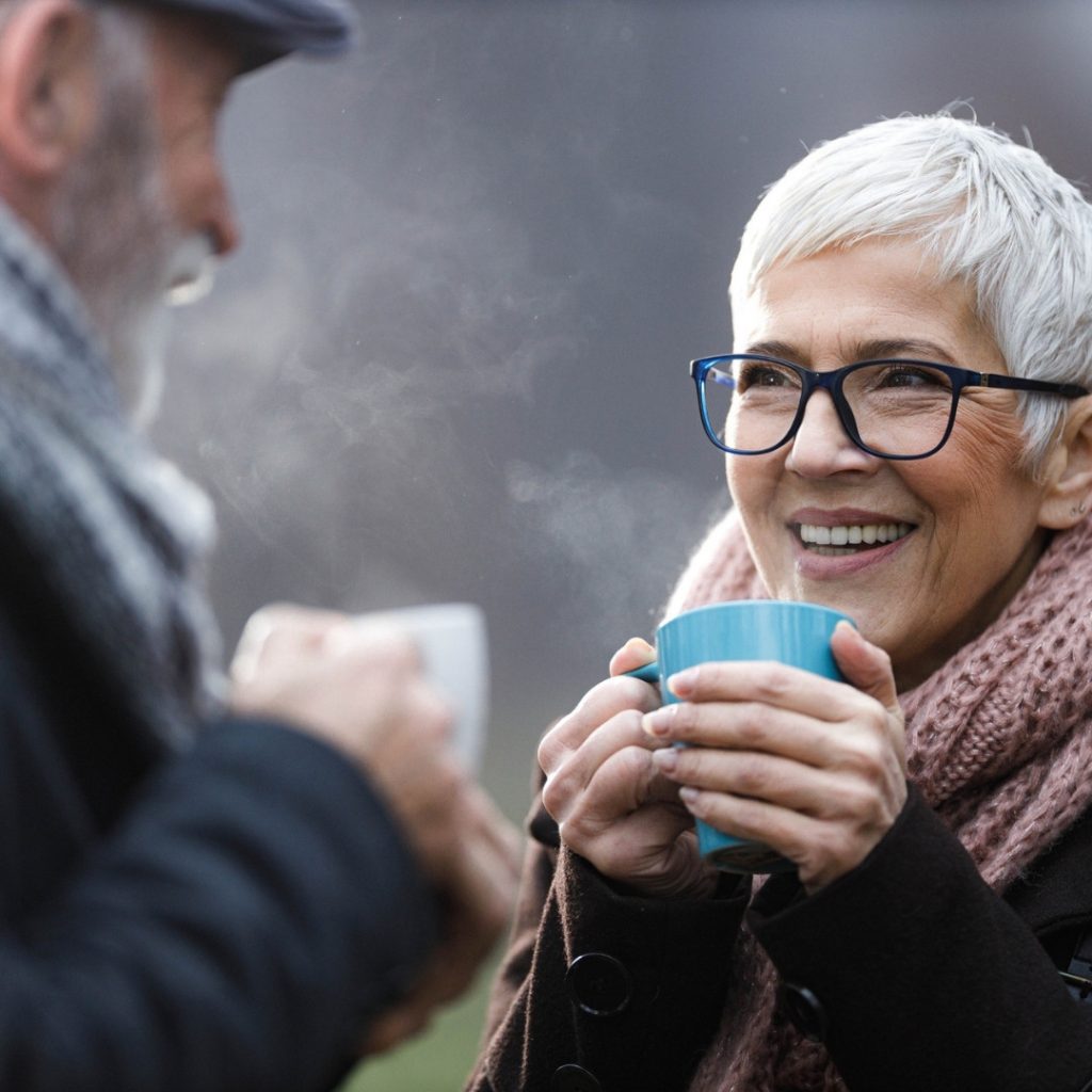 Elderly couple outside in the cold enjoying a hot drink.